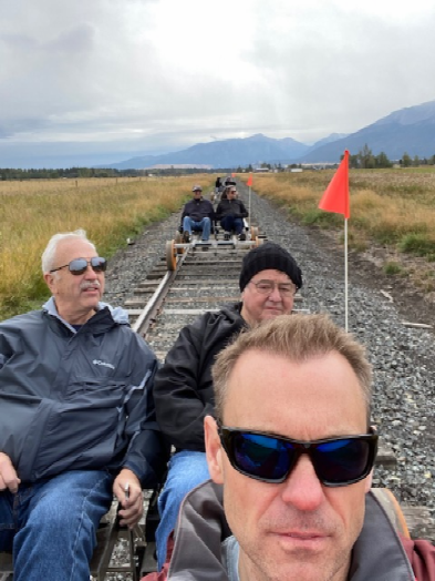 People riding pedal cars on railway at the base of a mountain.